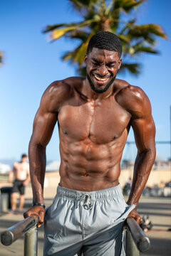 Man exercising outdoors on parallel bars, palm trees in background.