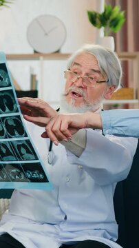 Healthcare concept where adorable worried adult blond woman discussing with skilled mature grey-bearded medical specialist her x-ray scan when medic visiting her at home