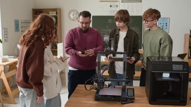 Tilt up zoom out shot of group of gathered students examening plasitic piece, printed on 3D printer during practical modeling lesson in modern school