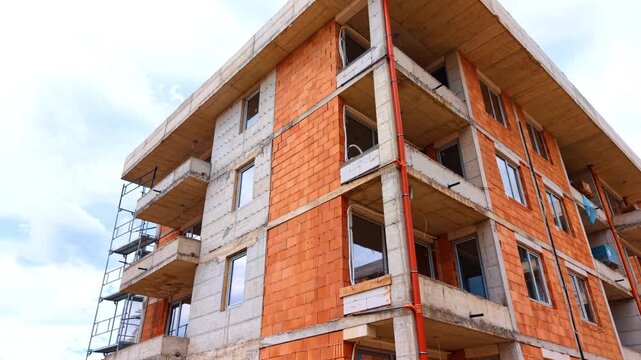 Low angle view of multi story residential building construction. Corner perspective of unfinished apartment house with brick walls and concrete balconies