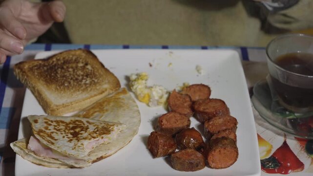 Person pricking roasted pork sausage pieces with a fork during a savory morning meal