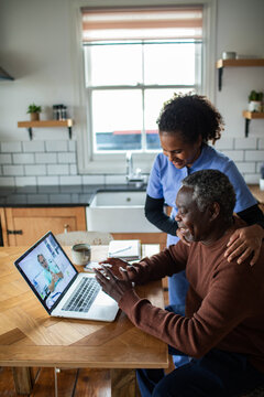Senior man and caregiver on telehealth video call at home kitchen
