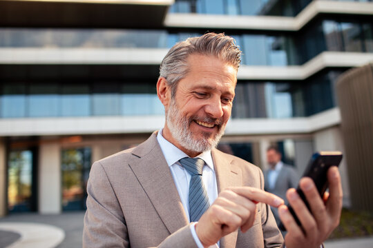 Smiling senior businessman using smartphone outside office
