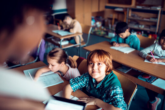 Happy elementary student looking at teacher in classroom