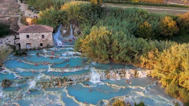 Tuscany Italy wellness - Saturnia thermal springs cascading pools drone view with people relaxing at sunset. Cascate del Mulino natural SPA limestone terraces luxury travel