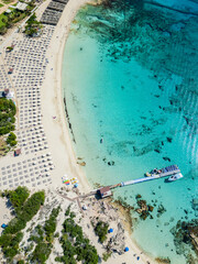 Obraz premium Aerial shot of a Makronissos beach in Ayia Napa, Cyprus, with crystal turquoise water, a wooden pier,