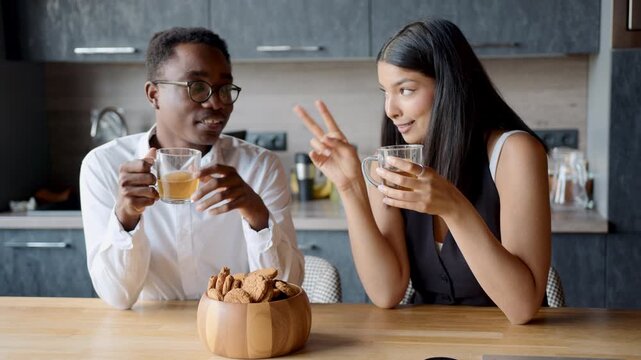 Black man and mixed race woman enjoying a delightful office break with cookies and tea, connecting with diverse colleagues in a relaxed atmosphere filled with laughter and conversation