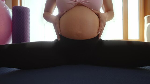 Beautiful pregnant woman practicing pilates exercises with a fitness ball in her living room, promoting health and well-being during pregnancy