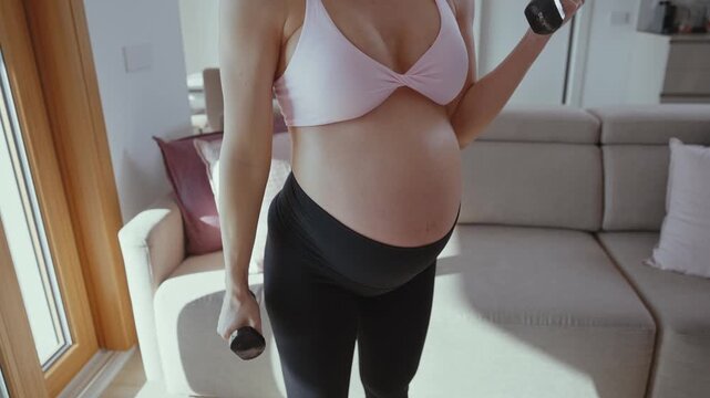Beautiful pregnant woman practicing pilates exercises with a fitness ball in her living room, promoting health and well-being during pregnancy