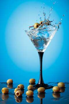 Martini with green olives on a wet table.