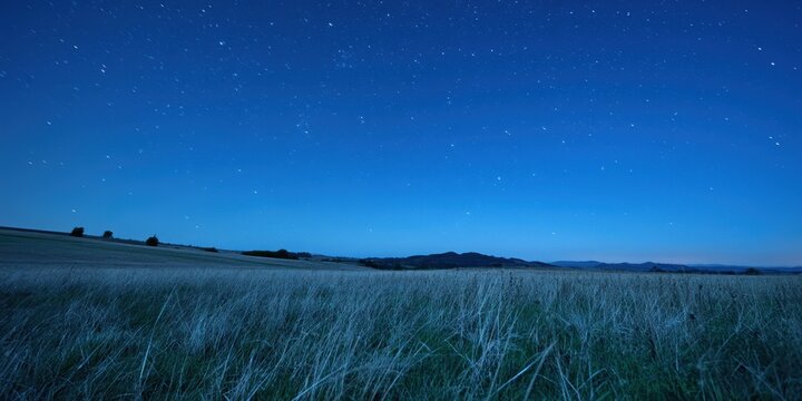 The Field Beneath a Starry Blue Night Sky with Distant Rolling Hills