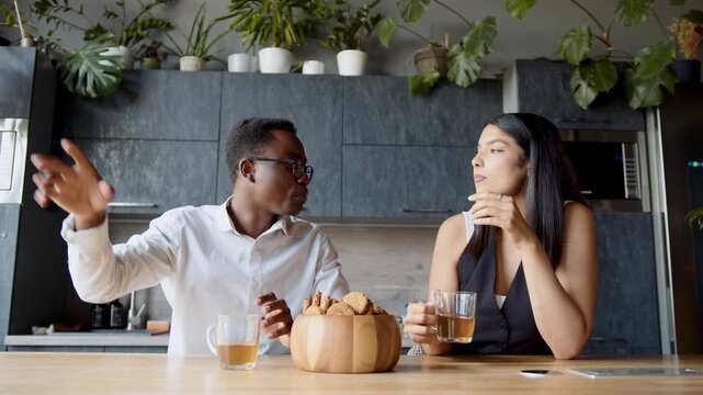 In a lively office setting, a black man and a woman enjoy a pleasant break together, sharing tea and cookies while engaging in lighthearted discussions about their work and life