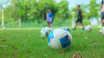 Fototapeta premium Soccer ball on green grass field with blurred children playing in background and copy space for text.