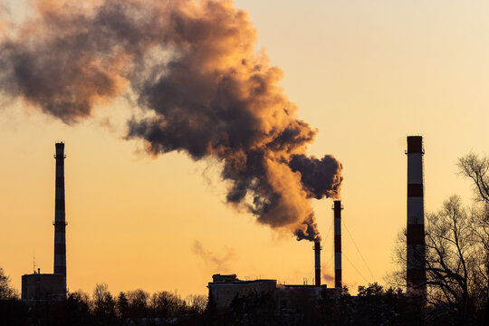 Industrial chimneys belching thick plumes of toxic smoke into the sunset sky, representing heavy air pollution, global warming impact, and environmental damage from massive power plant production