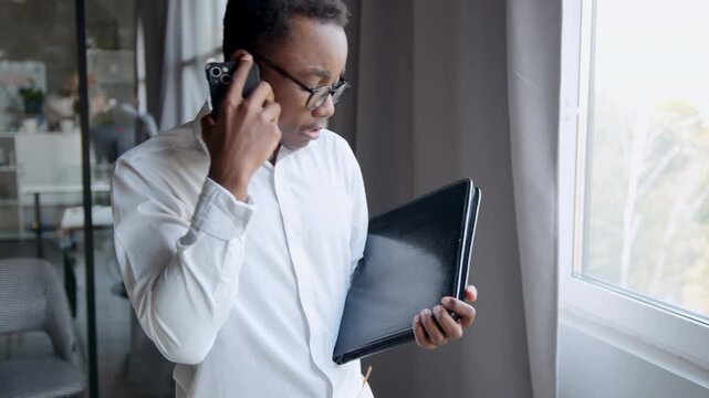 A man in an office is engaged in a heated discussion on his smartphone. He's balancing a folder in one hand while intently trying to make his point during a disagreement