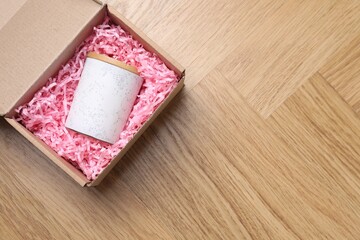 Fototapeta premium Cardboard box with shredded paper filler and candle on wooden table, top view. Space for text