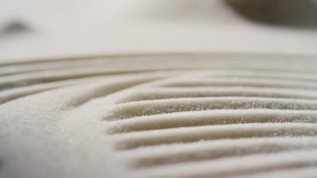 Slow motion tracking handheld tilt of rake raking sand forming ripple patterns on tabletop zen garden surface