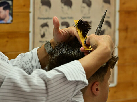Barber cutting clients hair with scissors and yellow comb