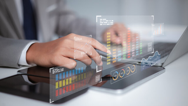 Businessman using tablet and laptop to analyze digital financial data charts with futuristic holographic interface.