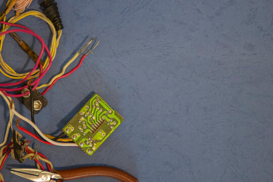 Reverse engineering and hardware repair concept. Green printed circuit board, wiring, and a hand tool forming a flat lay on a blue background with copy space.