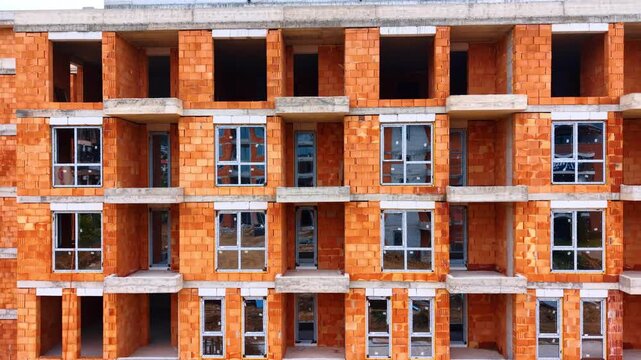 Red brick facade of residential building with installed windows. Front view of an apartment building facade built from red ceramic hollow bricks with glass windows and balconies.