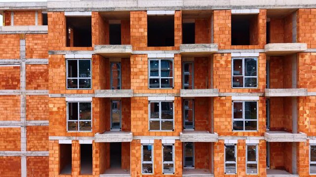 Unfinished multi story residential building with red brick walls. Close up facade shot of a residential building under construction made of orange ceramic blocks and windows.
