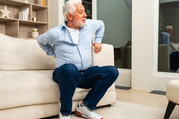 Obraz premium Backache back pain. Unhappy senior old man suffering from backache at home. Upset elder man feel sudden back pain muscles ache tension injury. Sad grandfather feeling pain hurt in back touching spine