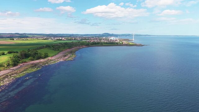 Scenic panorama of the Scottish coastline in Fife, featuring the blue waters of the Firth of Forth and a rocky shore with green fields under a bright summer sky.