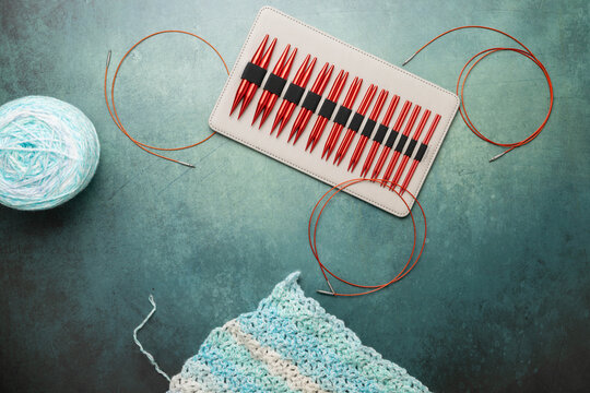 Set of interchangeable, circular knitting needles on green surface.