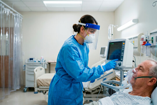 A professional healthcare worker in personal protective equipment monitoring a patient in a critical care hospital setting