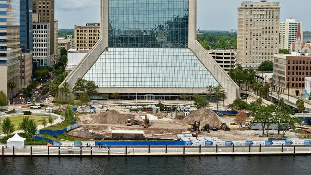 Aerial view of the Riverfront Plaza construction site with excavators and dirt piles in front of the Wells Fargo Center in Jacksonville, Florida, United States.