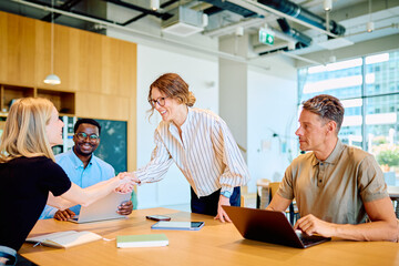 Diverse business people collaborating in a modern office, two women making a deal with a handshake, showing teamwork and partnership © we.bond.creations