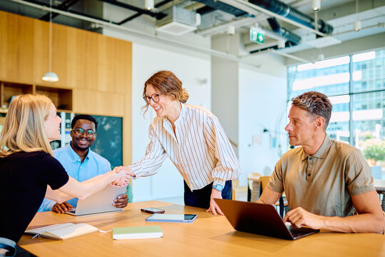Diverse business people collaborating in a modern office, two women making a deal with a handshake, showing teamwork and partnership