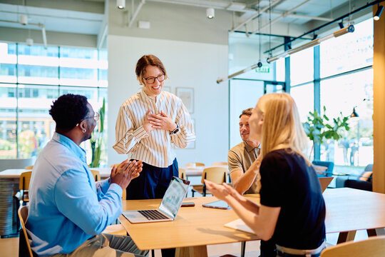 Group of diverse business professionals applauding and showing appreciation to a happy female team member during an office meeting