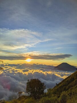Golden sunset over sea of clouds with Mount Sindoro silhouette view from Mount Sumbing hiking trail in Wonosobo Central Java Indonesia. Epic mountain landscape.