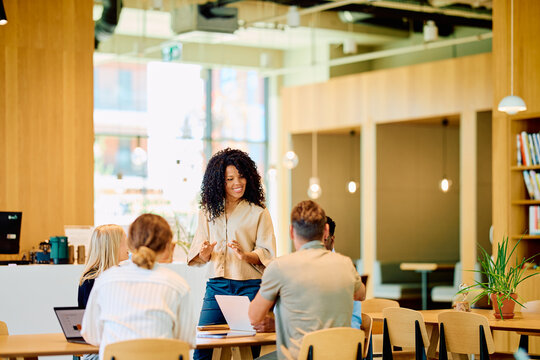 Diverse business team collaborating and discussing a project in a bright open-plan office space. Woman manager presenting to colleagues
