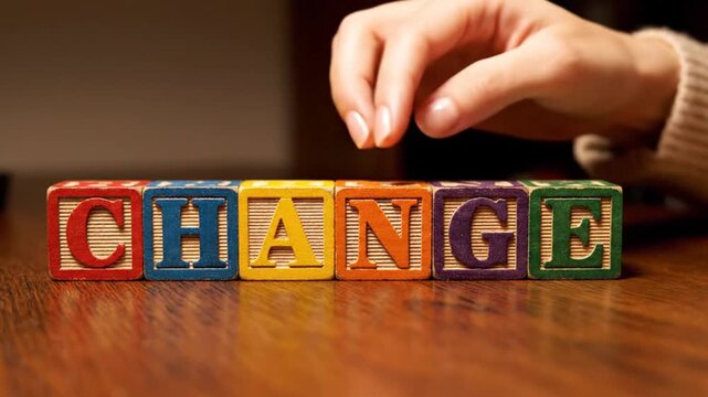 A hand arranges colorful wooden blocks to spell out the word change