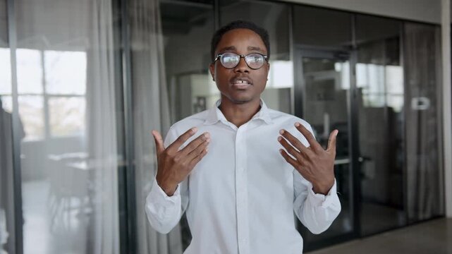 Black male speaker in white shirt with glasses presents a startup project pitch during an important business meeting in a modern office environment