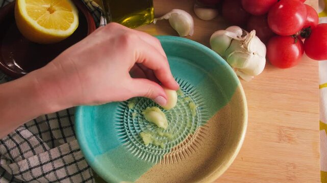 Hand grating fresh garlic on a ceramic garlic grater plate. Traditional Spanish ajo rallador or plato rallador used for preparing natural ingredients in Mediterranean cuisine. High quality 4k footage
