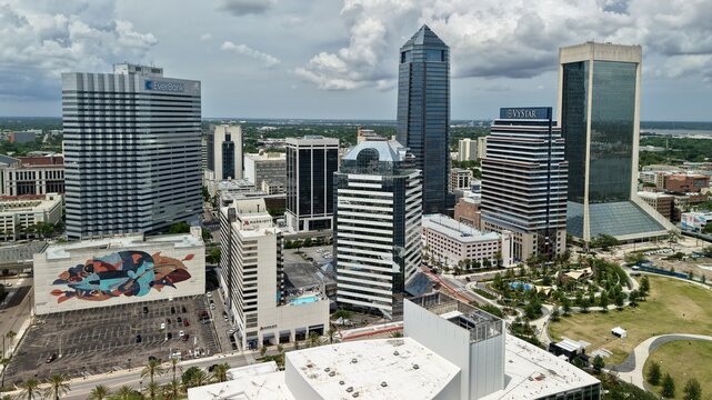 Aerial view of Riverfront Plaza and the modern downtown skyline with skyscrapers and a colorful mural under a cloudy sky in Jacksonville, Florida, United States.