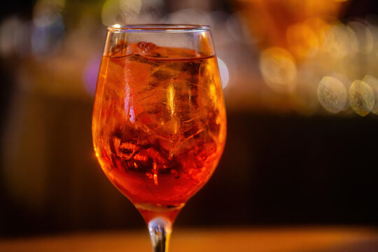 An aperol spritz drink on a glass at a lively bar during the evening with defocused background