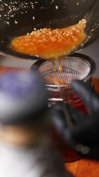 Chef colando aceite de jam&oacute;n ib&eacute;rico en un frasco de vidrio. Chef profesional filtrando la grasa de jam&oacute;n derretida en un frasco. Cocina artesanal espa&ntilde;ola, proceso tradicional.