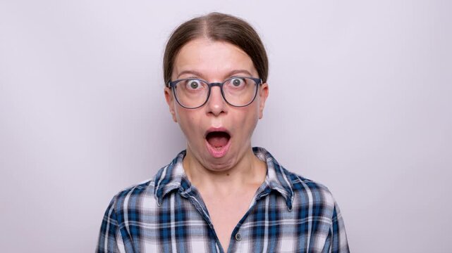 Shocked woman with wide open mouth looking at camera against white background. Surprised female in eyeglasses expressing amazement and disbelief during portrait shooting.