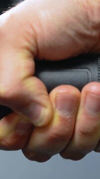 Vertical video: Pinching thumb on spotting hangnail, removing it at gray backdrop with black grip