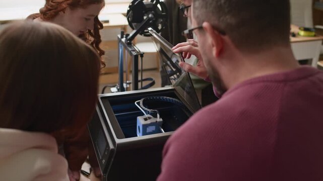 Close up over the shoulder shot of teacher showing focused students inner workings of 3D printer during practical lesson in school