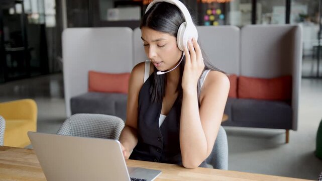 Indian woman providing customer service support from a modern office, actively engaging with clients through her headset and laptop during daytime