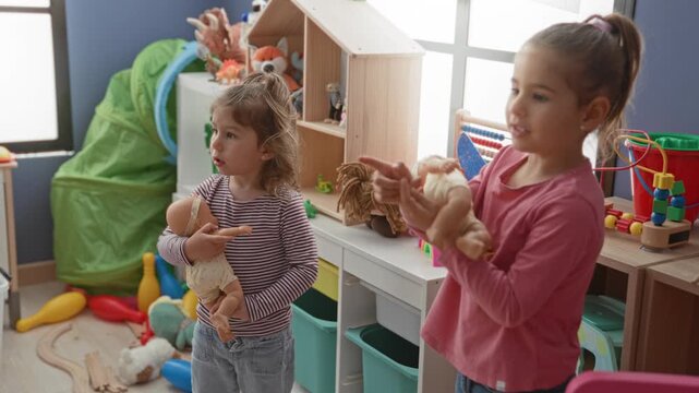 Girl holding a baby doll in a toy filled playroom with shelves, bins and a wooden dollhouse while two children share pretend caregiving; playful caring.