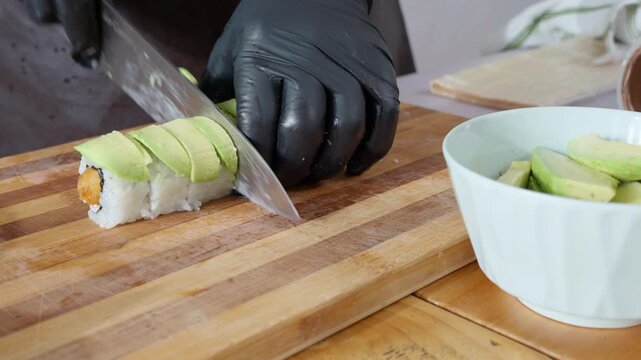 Chef cutting avocado covered sushi roll
