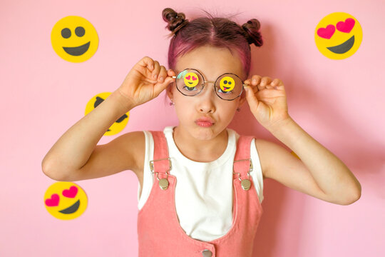 The girl lifts her glasses with emoticons pasted on the lenses, languidly pouting with negative emotions. World Emoji and Social Media Day.