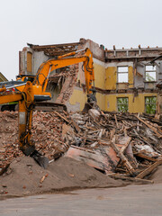 Fototapeta premium Excavator demolishing abandoned brick building with rubble and timber debris at construction site